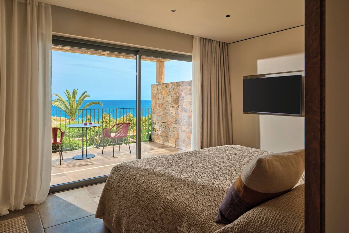 Een slaapkamer met een groot bed, een aan de muur bevestigde televisie en een balkon met uitzicht op de oceaan.