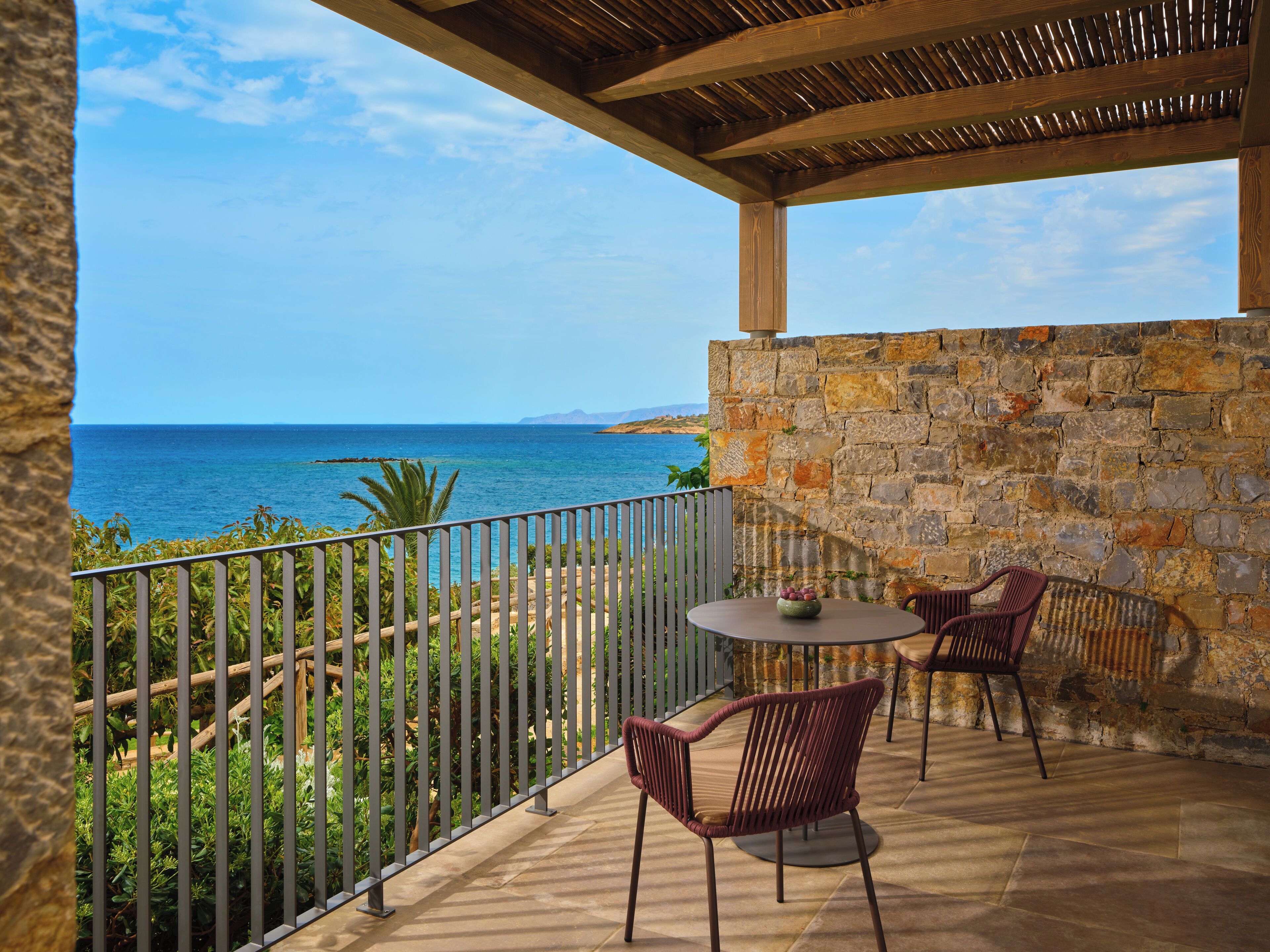 A balcony with a stone wall, a view of the sea, and two chairs.