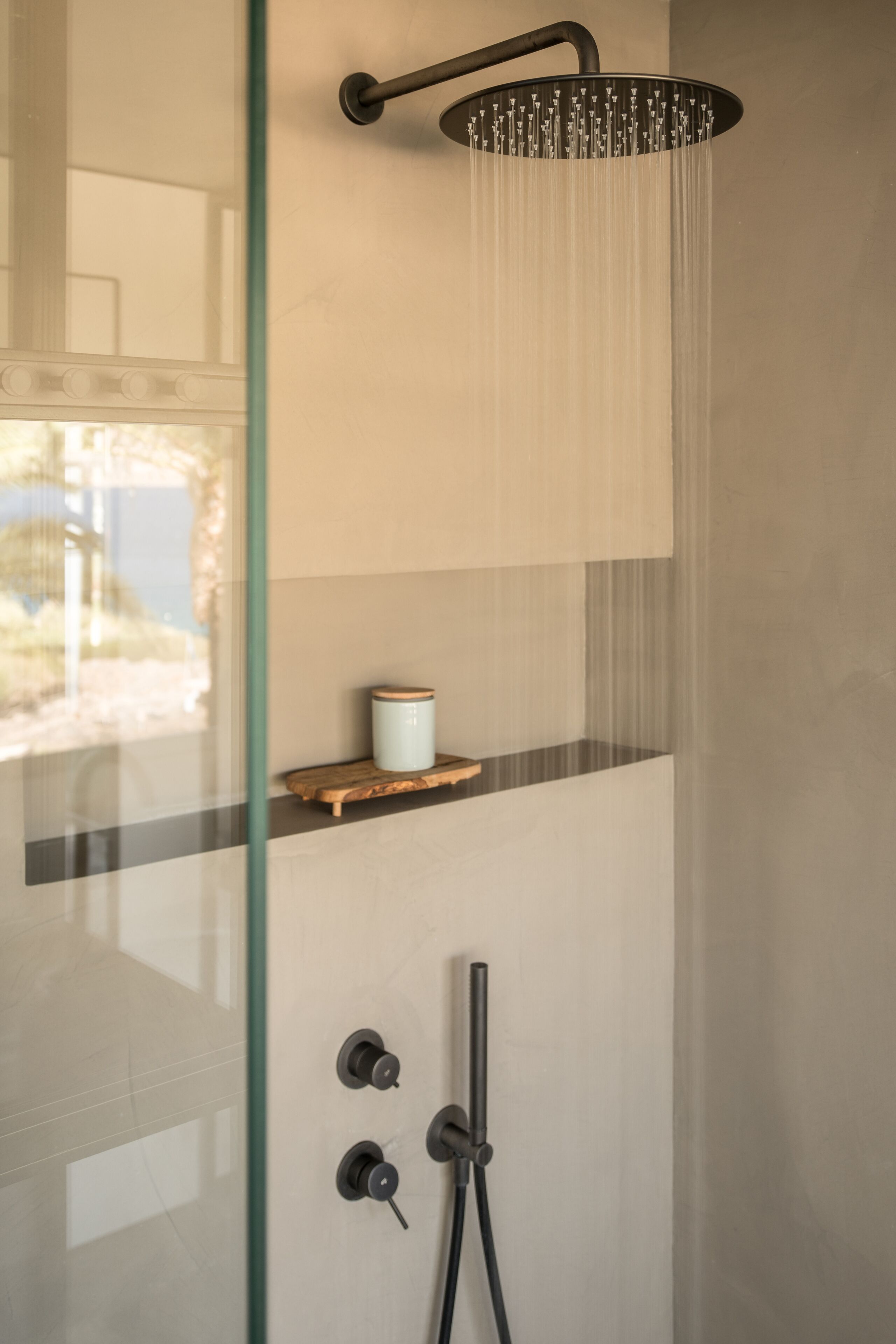 Een moderne douche met een glazen cabine, een houten plankje met een bakje, en een bedieningspaneel.