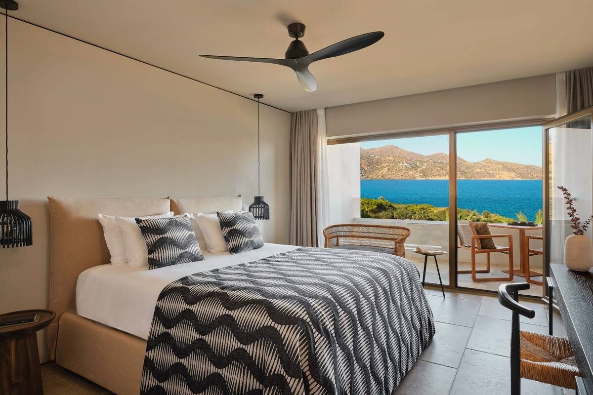 Een slaapkamer met een groot bed, een plafondventilator en uitzicht op zee.