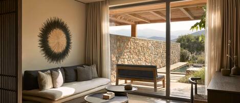 Una sala de estar moderna con un sofá, dos mesas de centro y vistas a un muro de piedra y un área de estar al aire libre.