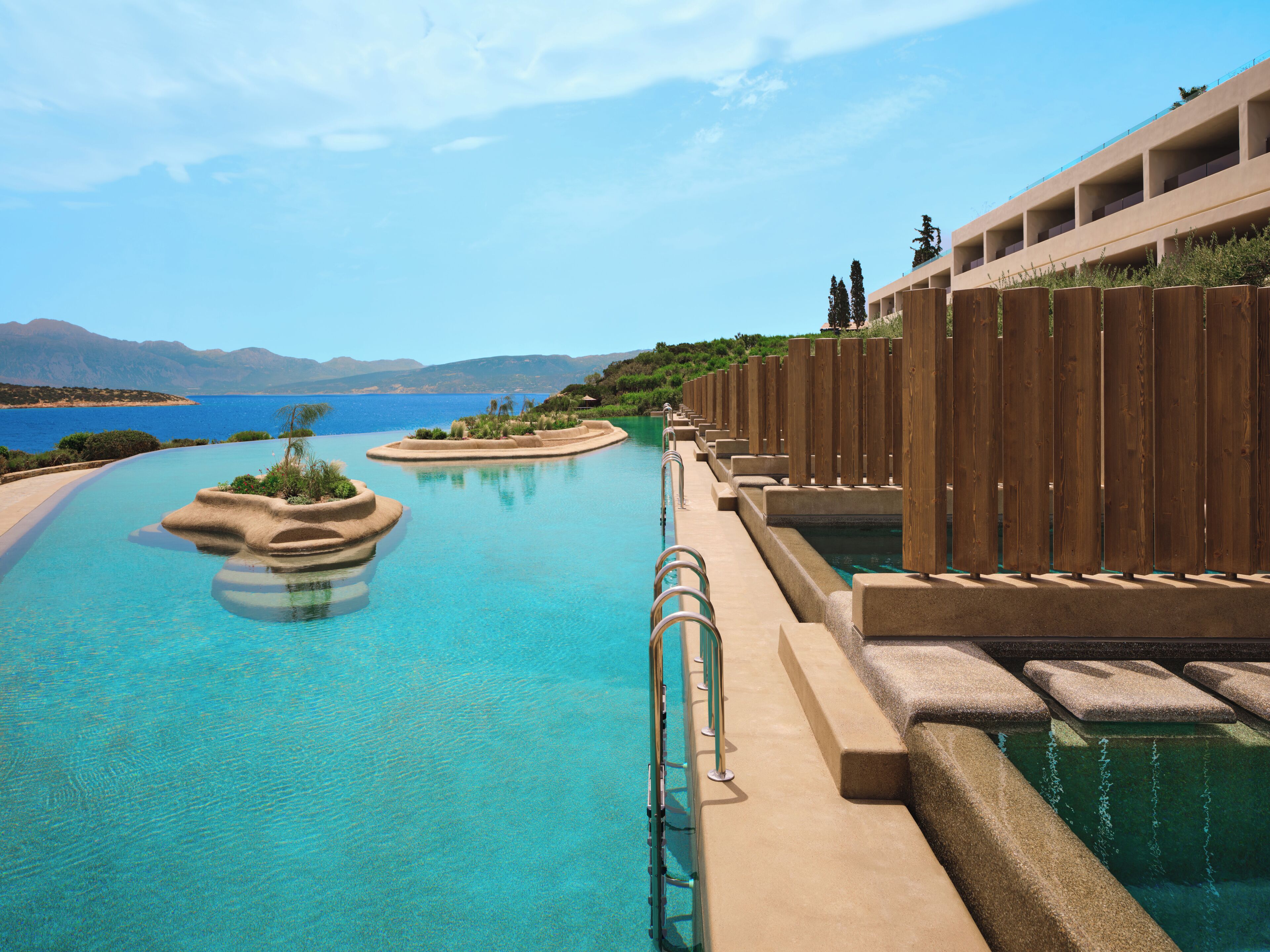 Une piscine avec une terrasse en bois, une vue sur la mer et des montagnes en arrière-plan.