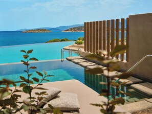 Ein Pool ohne Ende mit Blick auf das Meer und Hügel, ein Holzdeck und ein Steinweg, der zum Pool führt.