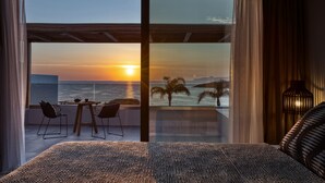 Een slaapkamer met een grote schuifglazen deur die leidt naar een balkon met uitzicht op de ondergaande zon boven de oceaan.