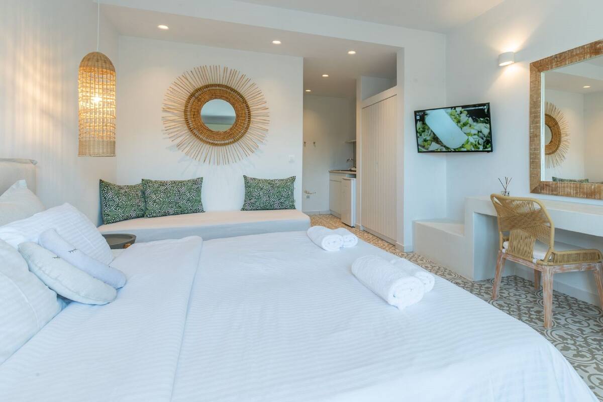 Una habitación de hotel con una cama grande, televisor, espejo y una silla de mimbre.