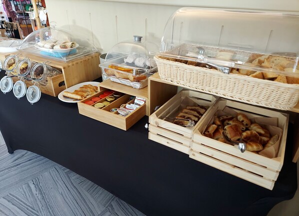 A buffet table with various food items, including pastries and sandwiches, displayed in clear containers and baskets. - Adonis Hotel & Apartments (Paros)
