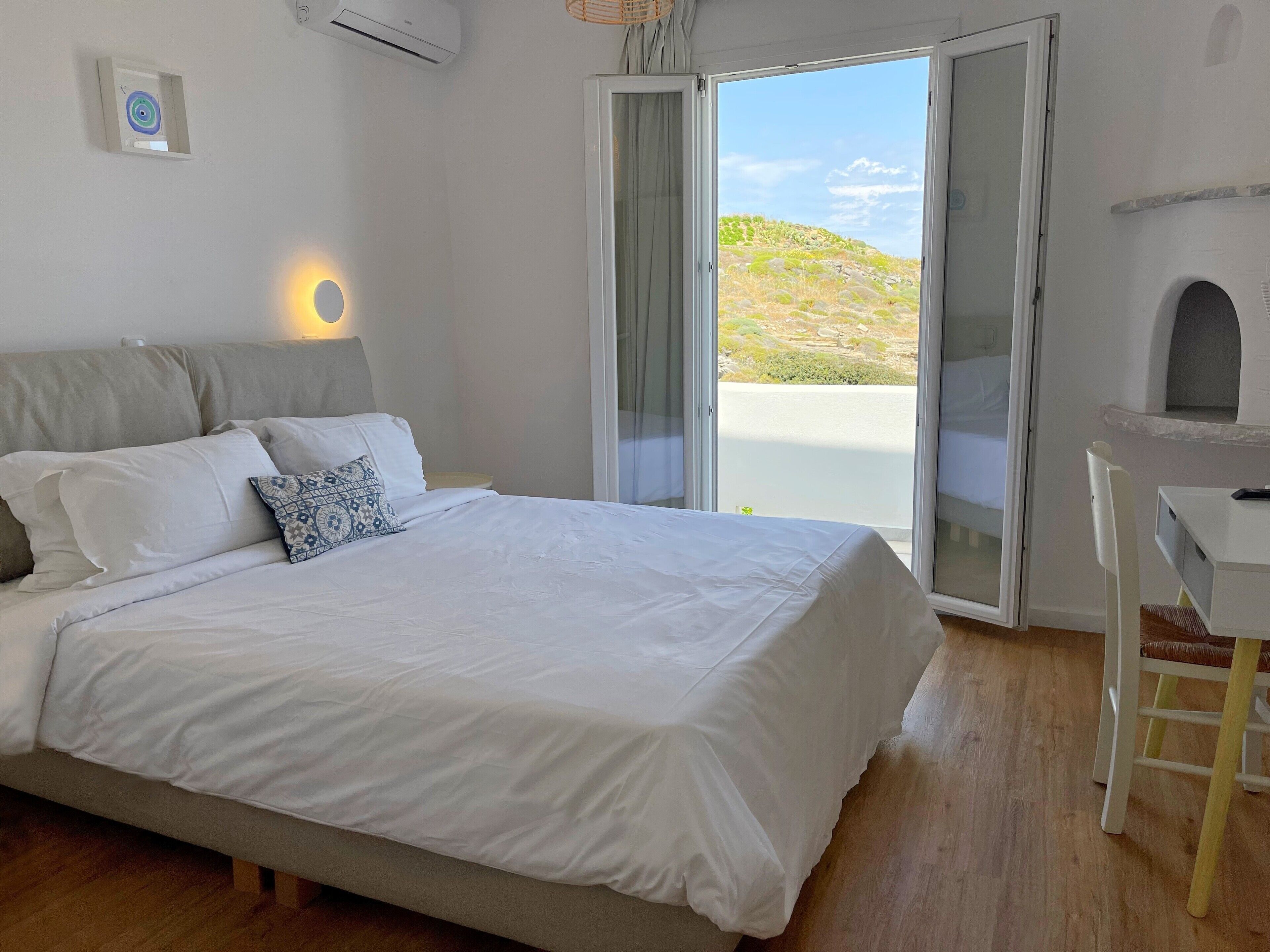 A bedroom with a bed, a bedside table, a chair, a desk, and a window with a view of a landscape.