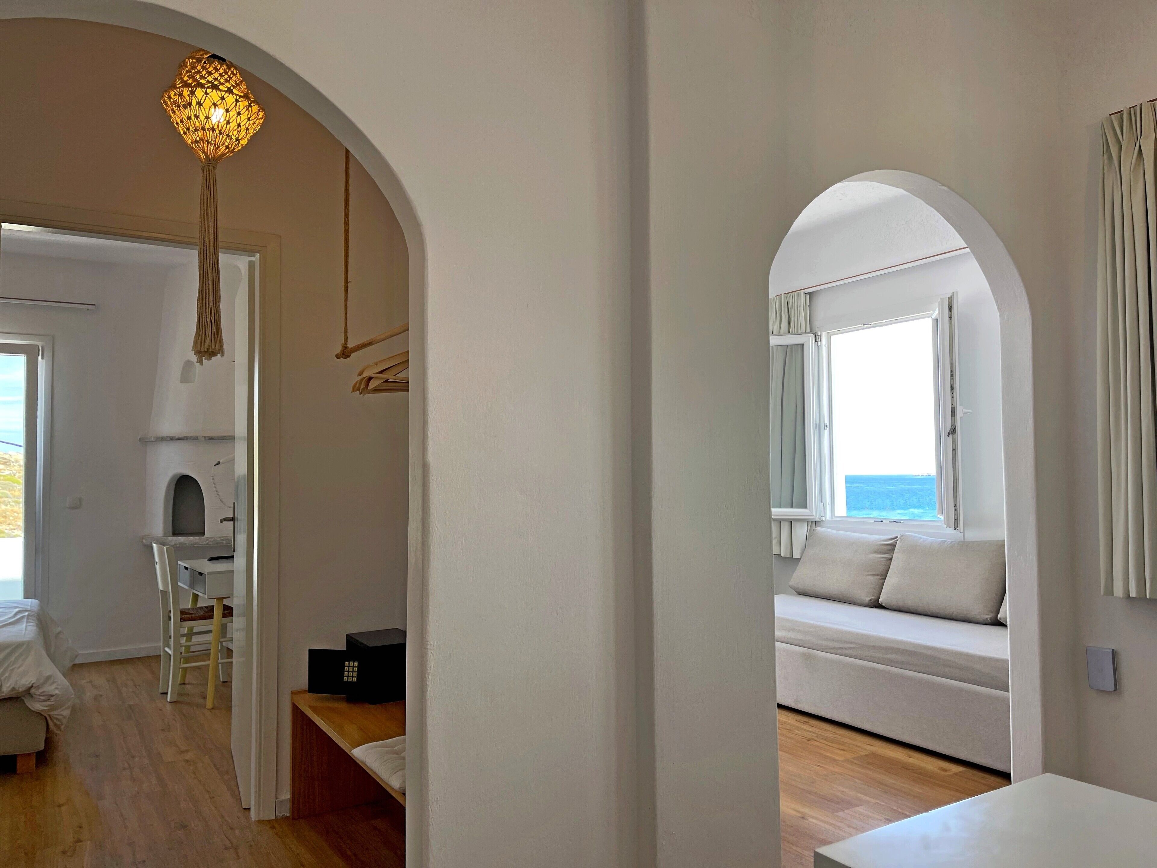 A modern room with a wooden floor, a white sofa with cushions, a small table, and a hanging light fixture.
