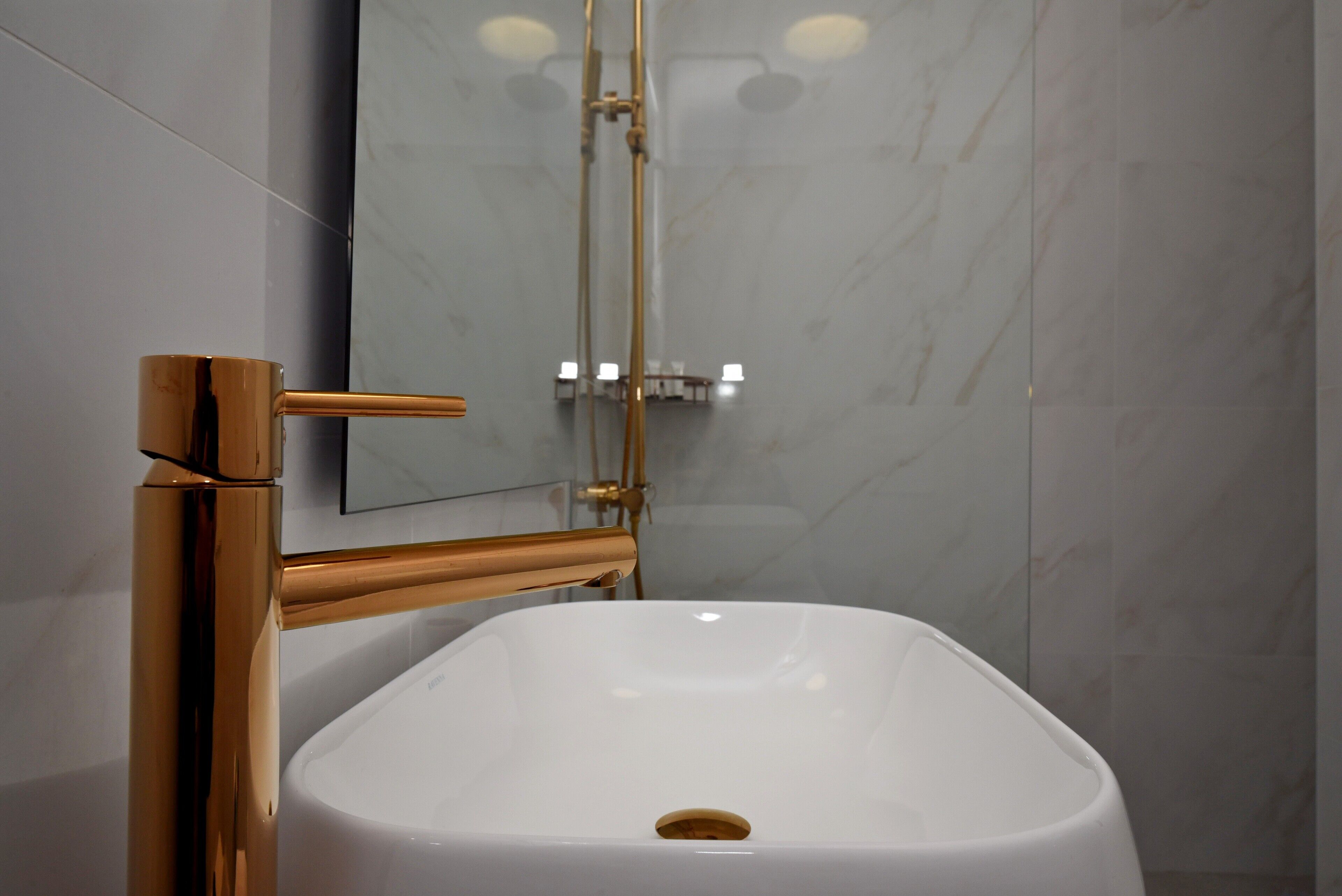 A modern bathroom with a white sink, gold fixtures, and a glass shower enclosure.