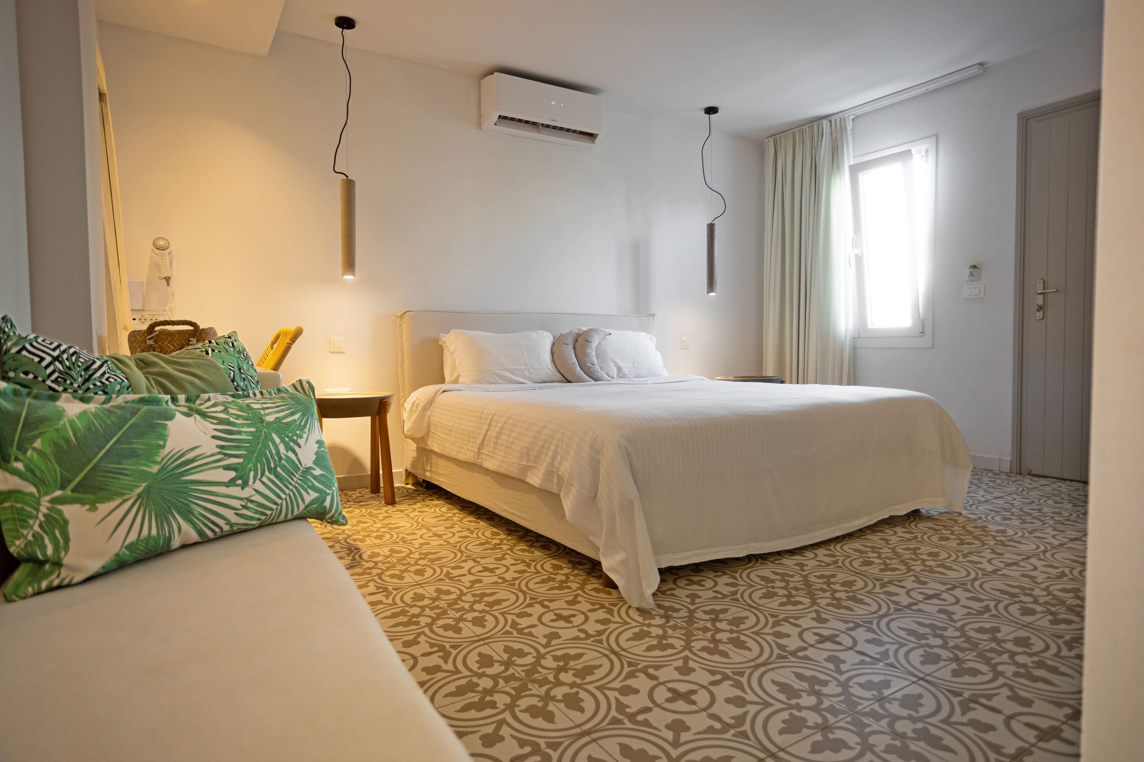 A bedroom with a bed, a bedside table, an air conditioner, a window with curtains, and a patterned floor.