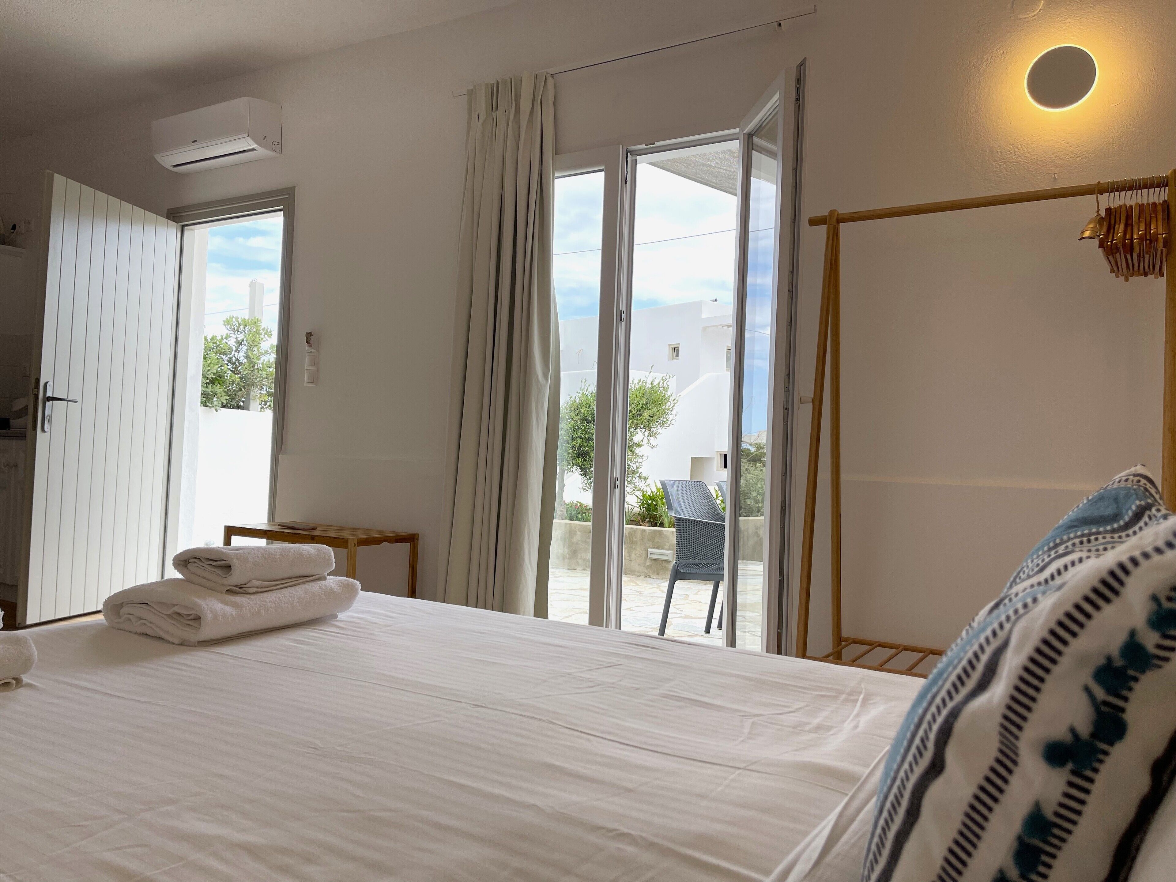 A hotel room with a bed, a window with curtains, a small table, and a chair.