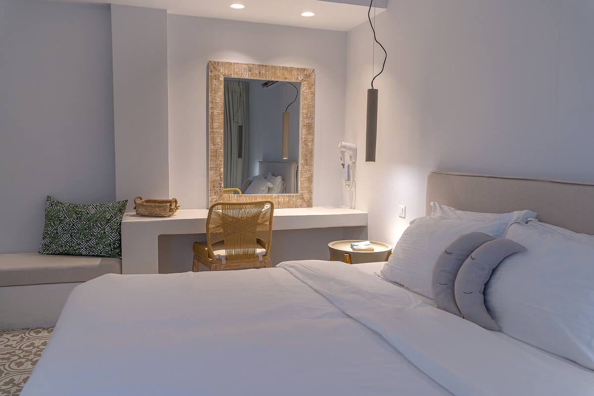 Un dormitorio moderno con una cama grande, una mesita de noche, una silla, un espejo y una pequeña mesa con una lámpara.