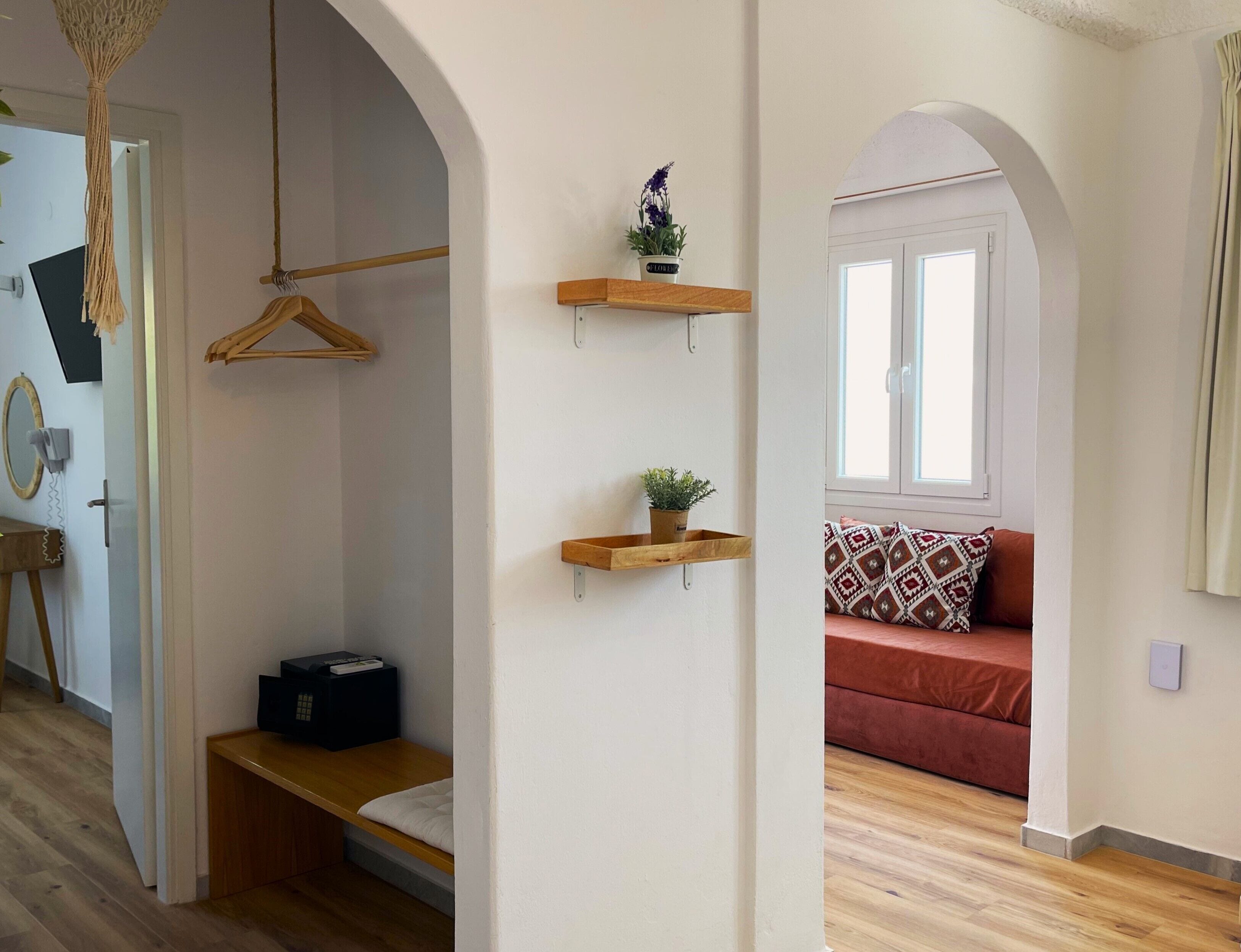 A room with a wooden bench, a hanging garment rack, and two wooden shelves with plants.