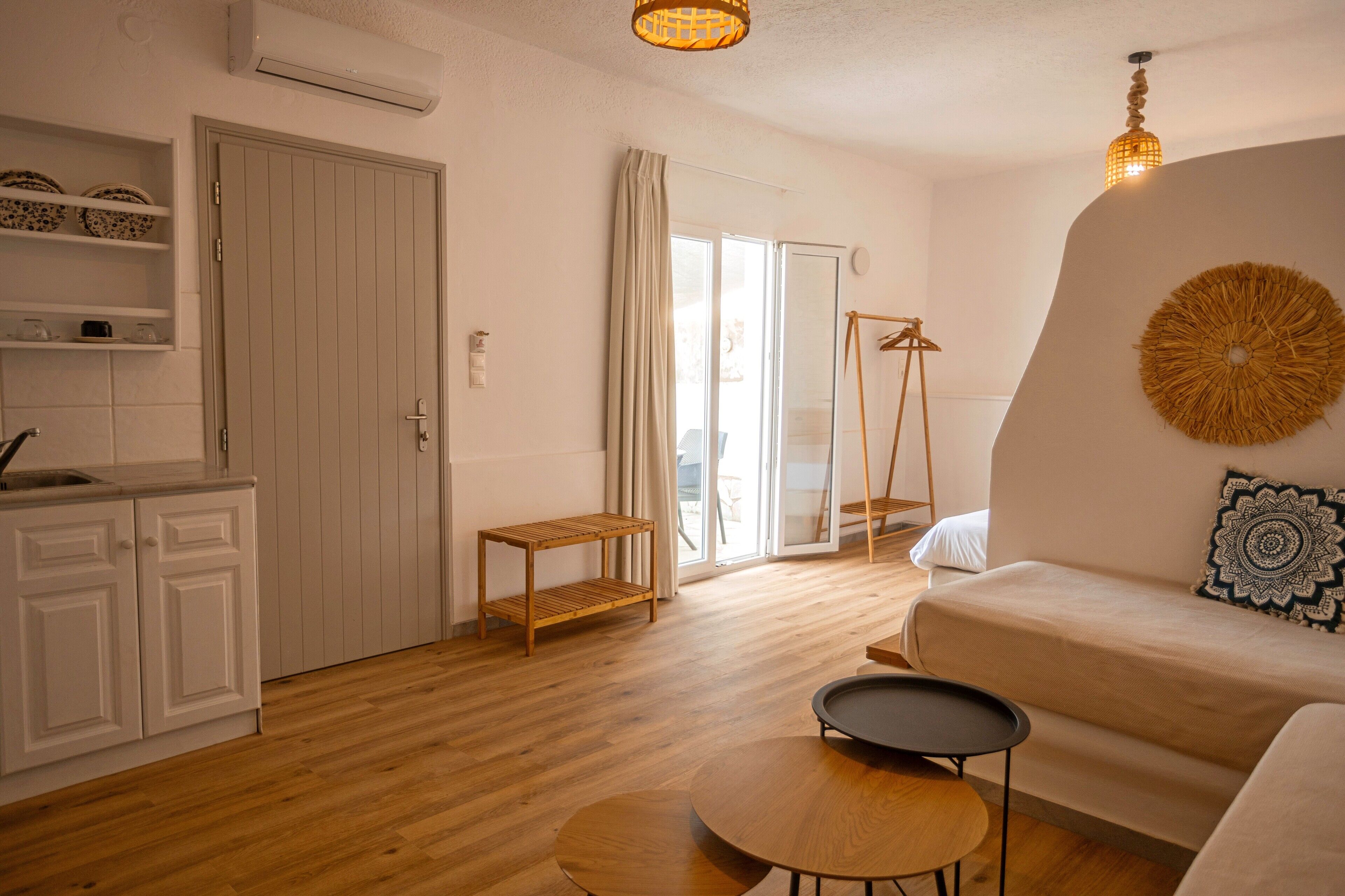 Een moderne woonkamer met een bank, een klein rond tafeltje en een houten bijzettafeltje. Er is een deur naar een balkon en een plank met decoratieve objecten.
