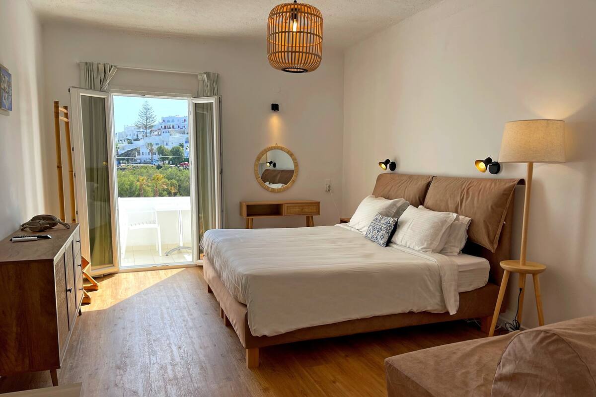Un dormitorio con una cama grande, una mesita de noche, una lámpara, un espejo y vistas al exterior.