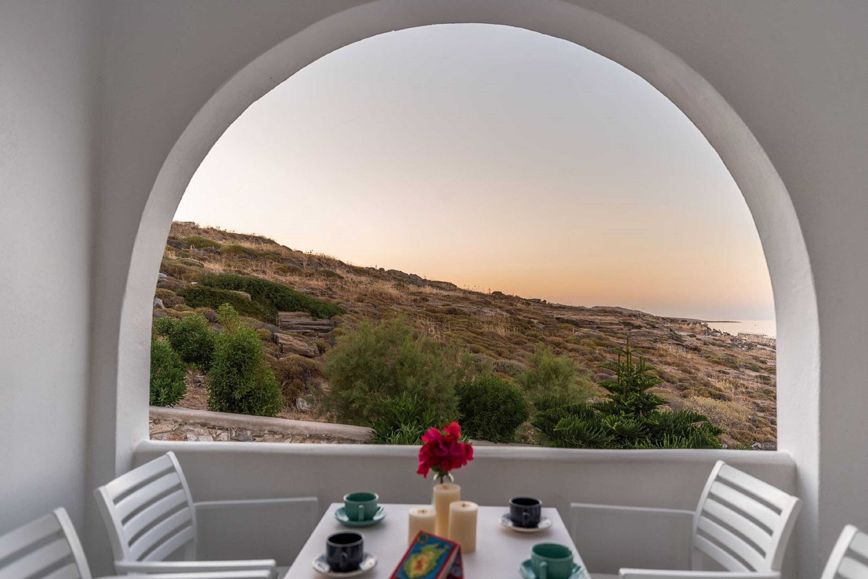 Een balkon met een tafel voor twee personen, met uitzicht op een rotsachtig landschap en de zee.