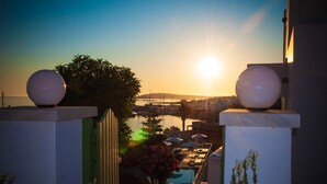 A view of a marina with boats, a sunset, and a pool area with umbrellas. - Adonis Hotel & Apartments (Paros)