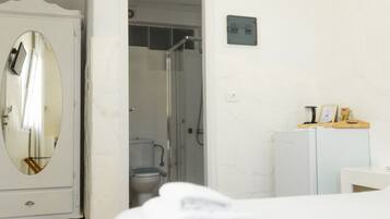 Habitación de hotel con cama, armario, espejo, zona de ducha y un refrigerador pequeño.