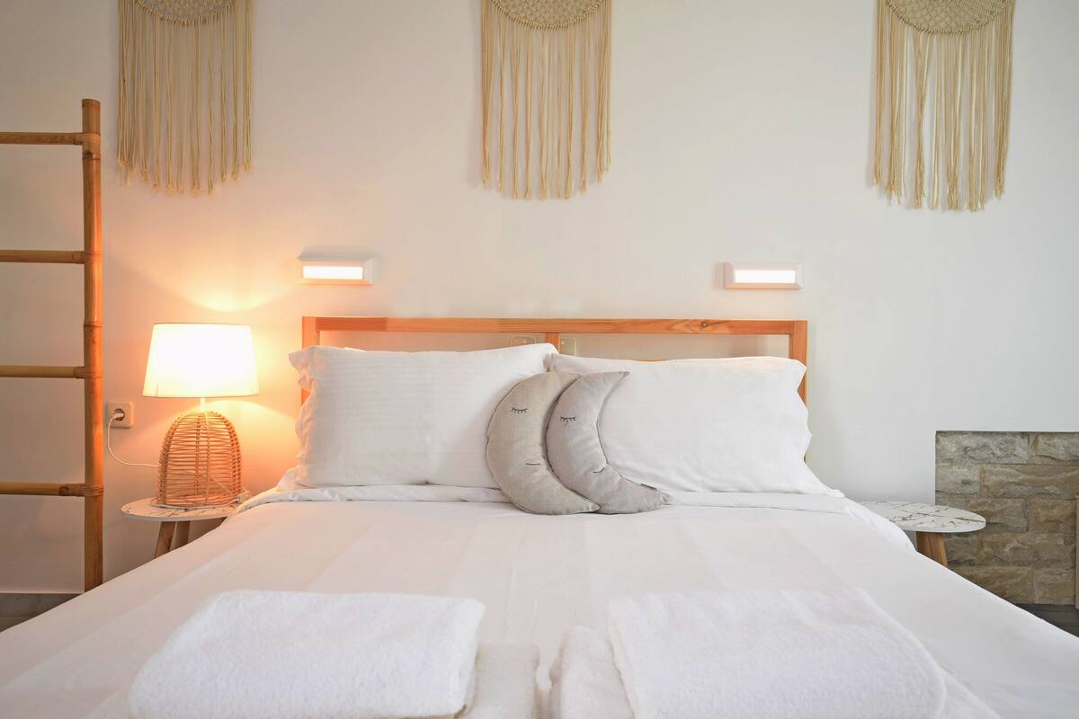 Una cama bien tendida con sábanas blancas, dos lámparas de noche y un cabecero de madera.