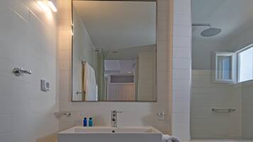 A modern bathroom with a large mirror, white tiles, a sink with two bottles, and a towel.