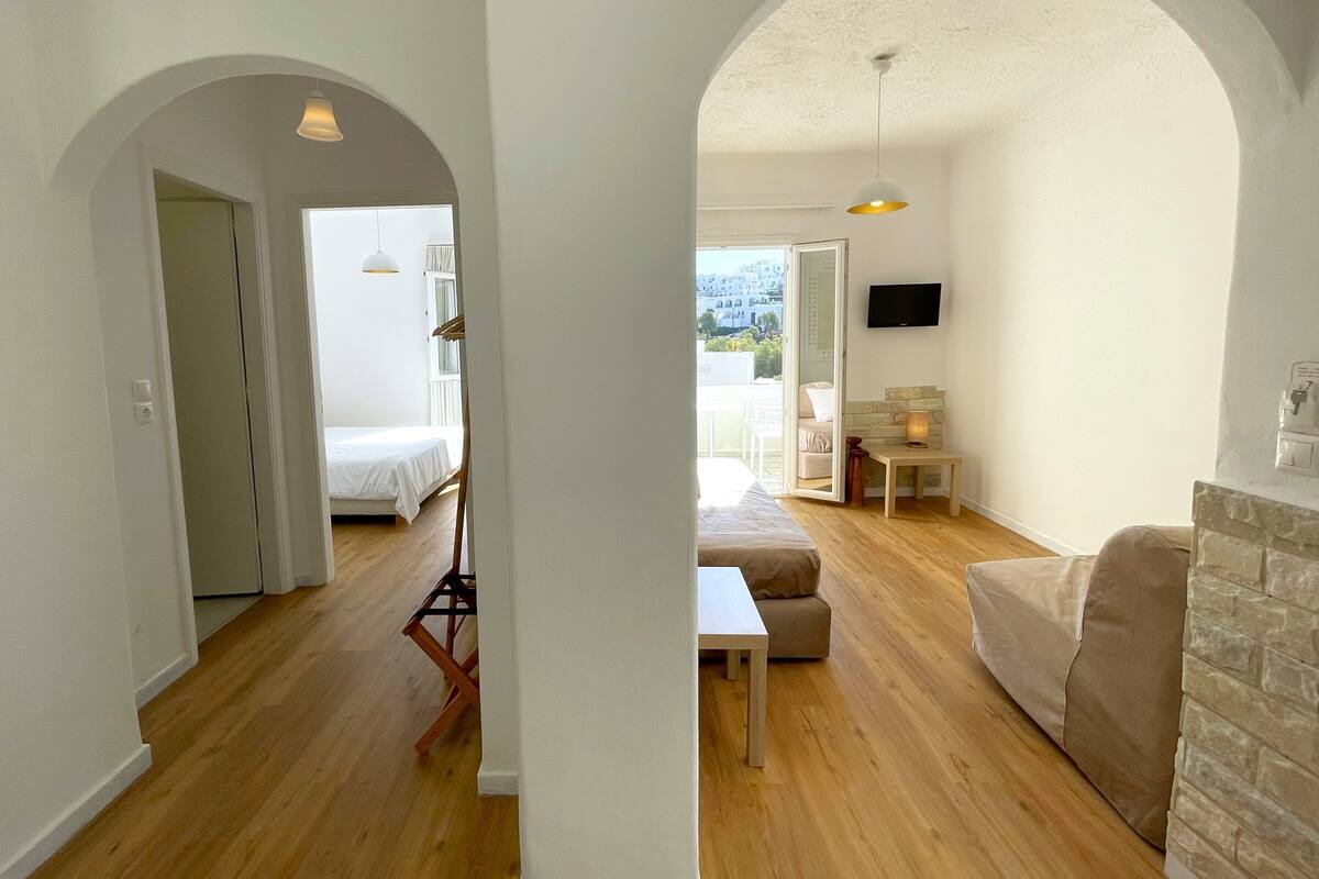 Amplia sala de estar con piso de madera, un sofá, una mesa y un televisor montado en la pared.