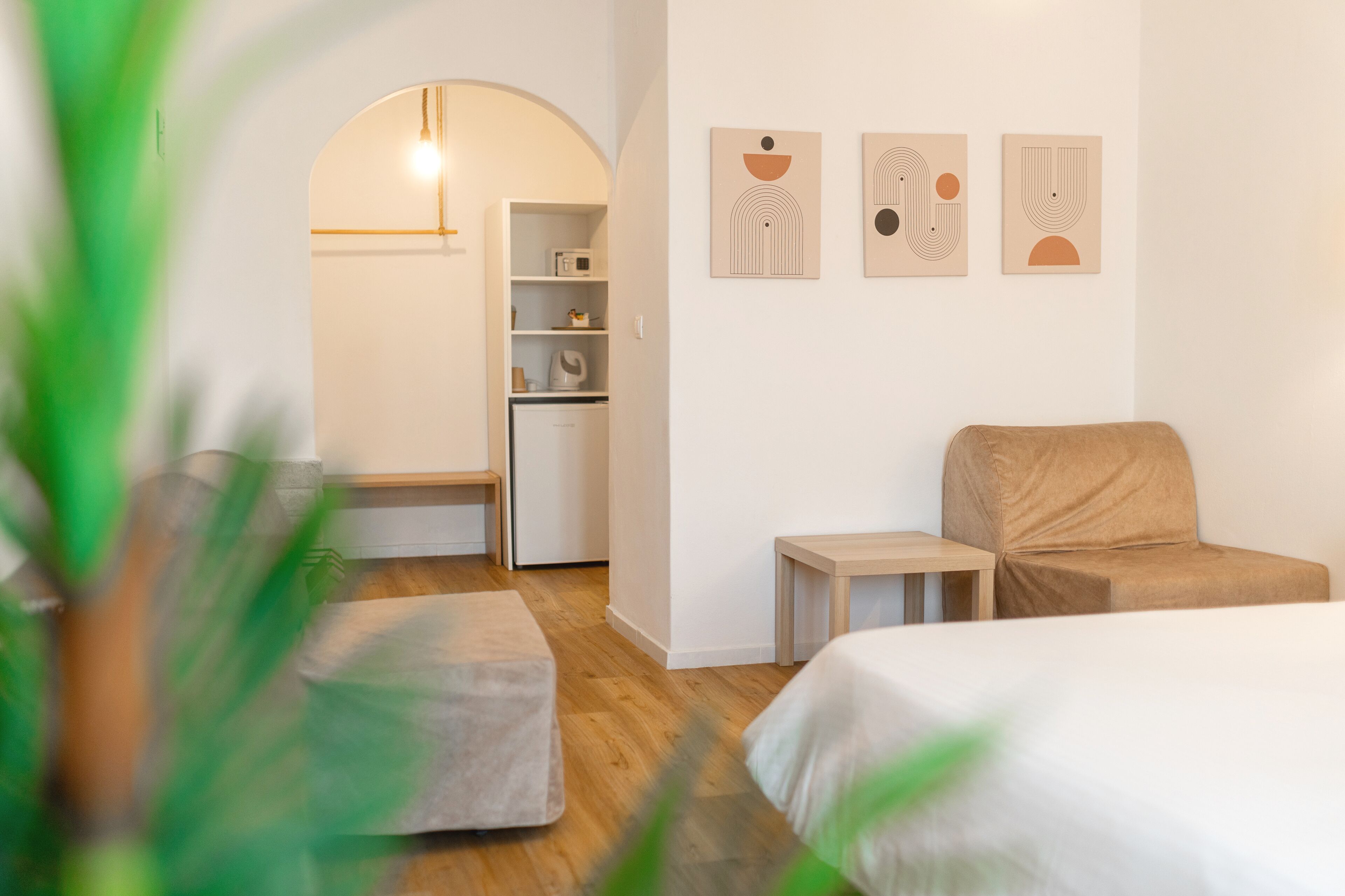 A modern hotel room with a wooden floor, a bed, a sofa, a small table, and a kitchenette.