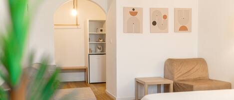 A modern hotel room with a wooden floor, a bed, a sofa, a small table, and a kitchenette.
