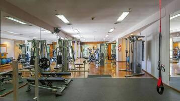 A gym with various exercise equipment, including weight machines and free weights, and a mirror wall.