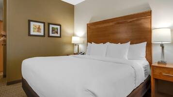 Habitación de hotel con una cama grande, cabecera de madera, dos lámparas de noche y dos cuadros en la pared.