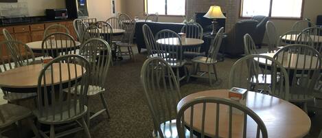 A dining area with round tables and chairs, a television mounted on the wall, and a brick wall.