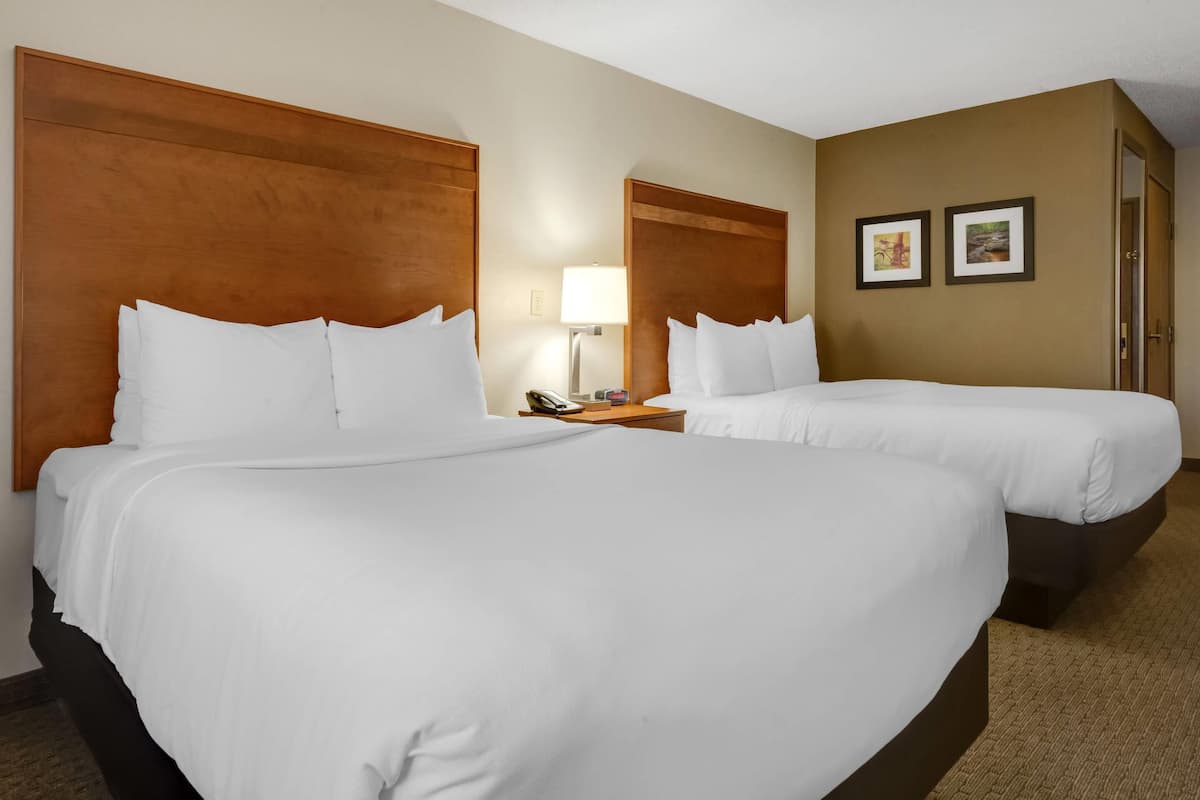 A hotel room with two beds, a nightstand with a lamp, and two framed pictures on the wall.