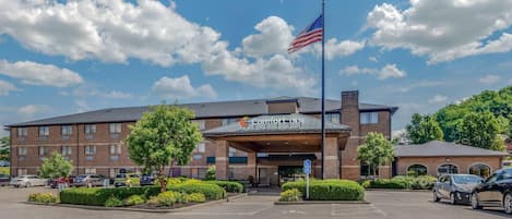 A hotel with a brick facade, American flag, and a parking lot with several cars.