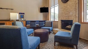 A lounge area with blue seating, a flat-screen TV, a fireplace, and a brick wall.