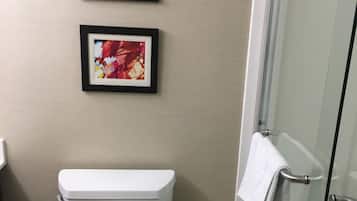 A bathroom with a white toilet, a framed picture of a landscape, and a glass shower door.