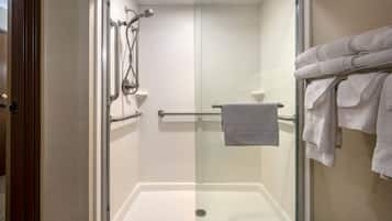 Ducha con mampara de vidrio, barra de apoyo, perchero con toallas y puerta a la izquierda.