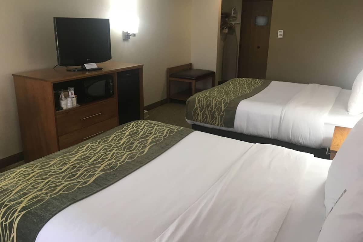 A hotel room with two beds, a TV on a wooden cabinet, and a desk with a chair.