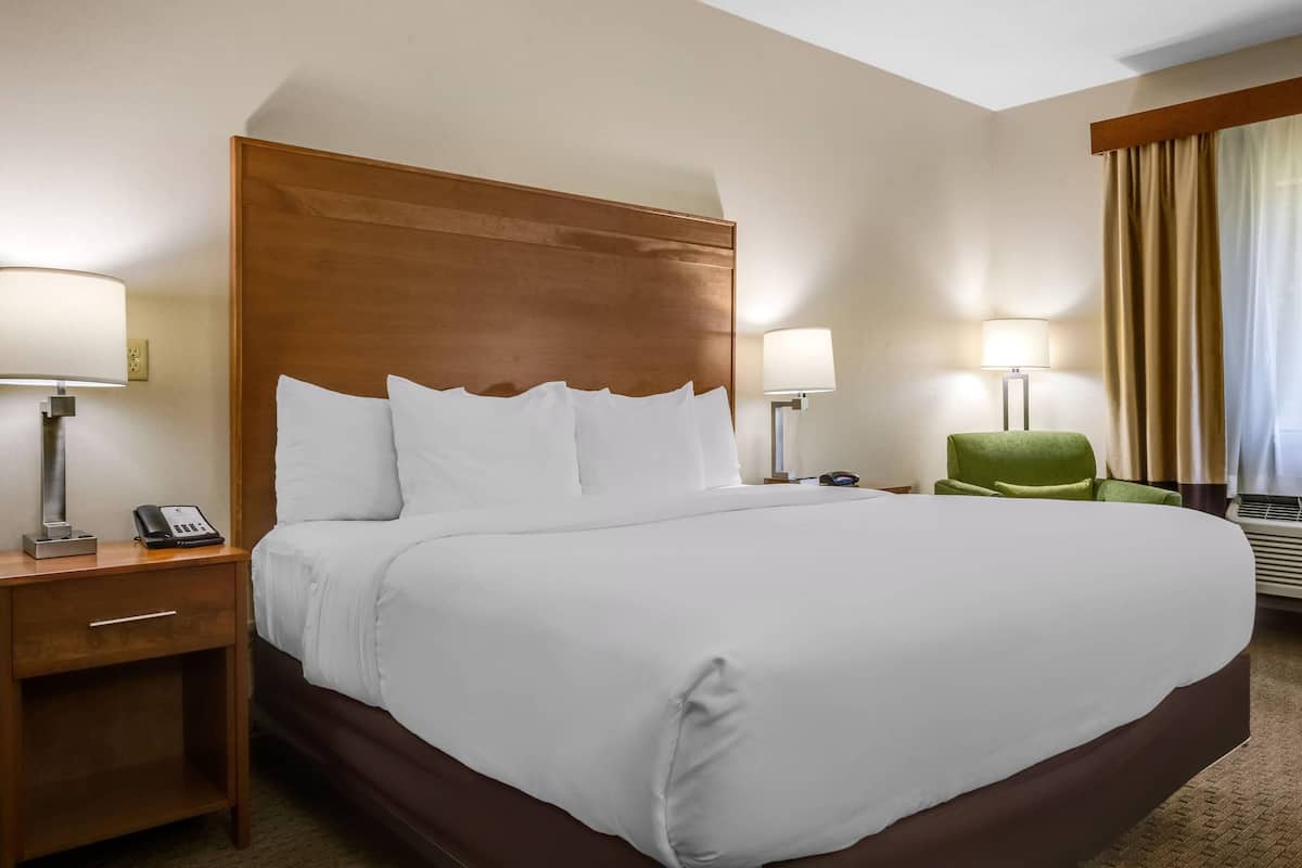 A hotel room with a large bed, two bedside tables with lamps, a green chair, and a window with curtains.