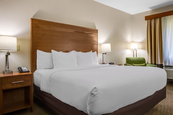 A hotel room with a large bed, two bedside tables with lamps, a green chair, and a window with curtains.
