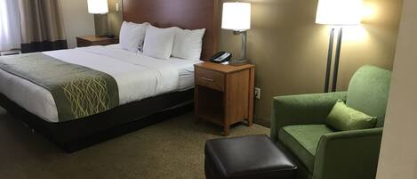 A hotel room with a bed, a desk, a chair, and two lamps.