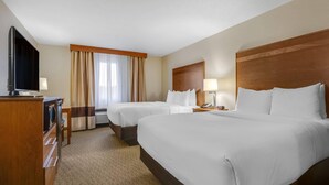 A hotel room with two beds, a TV, a desk, and a window with curtains.