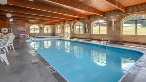 An indoor swimming pool with wooden beams, arched windows, and white chairs.
