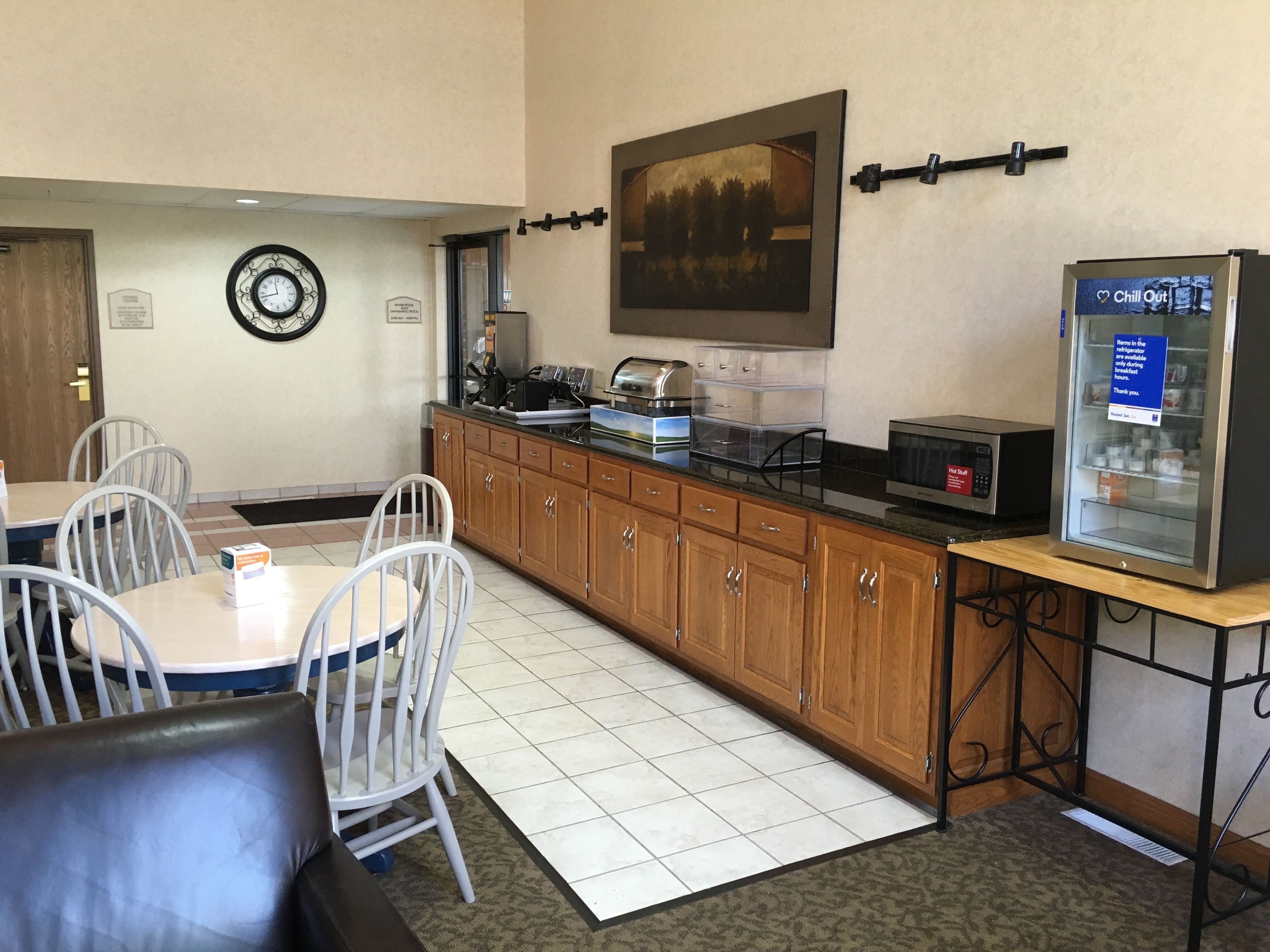 A small kitchenette with a refrigerator, microwave, and coffee maker. There are white chairs and a table in the dining area.