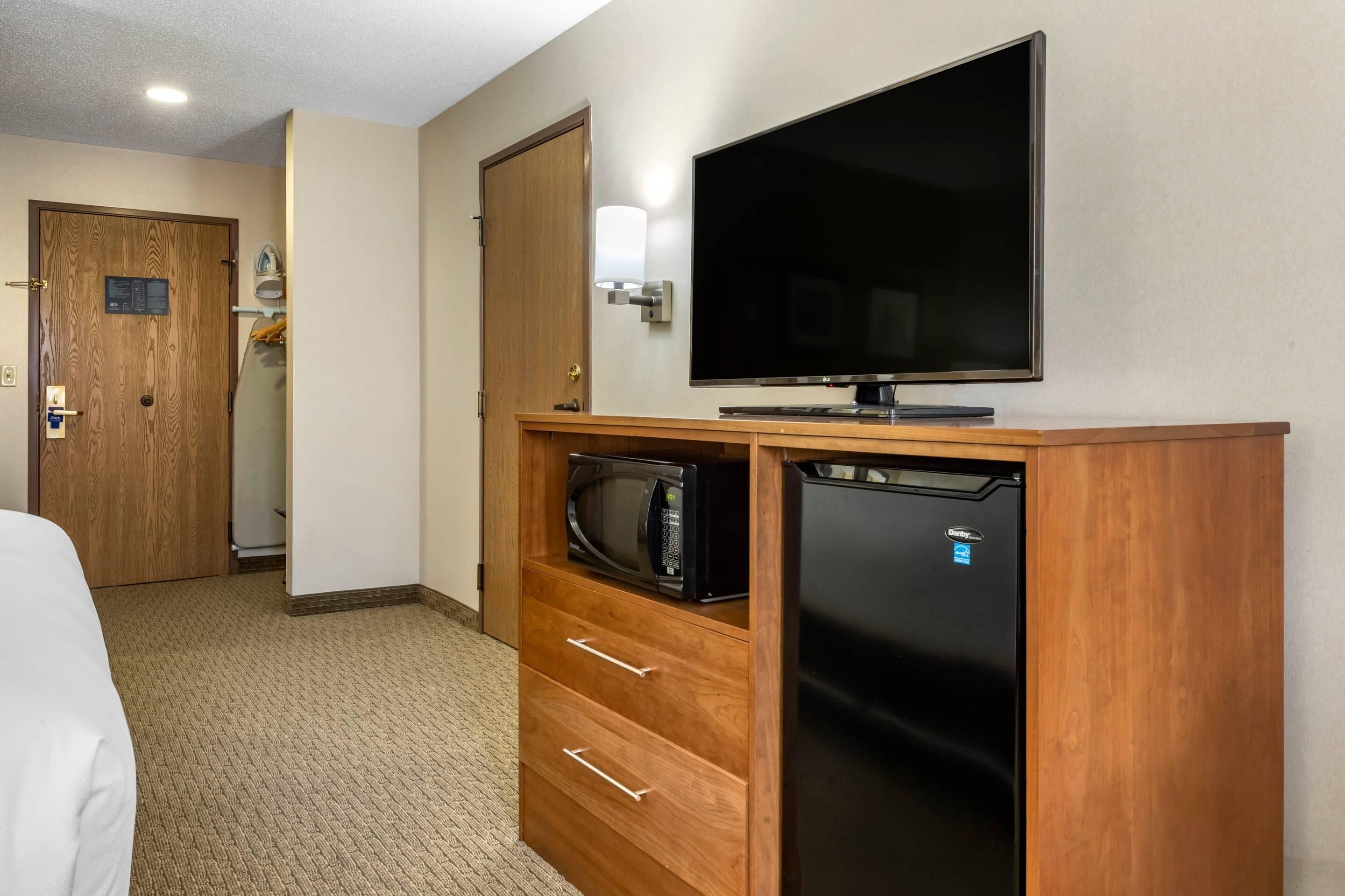 Habitación de hotel con un armario de madera, televisor de pantalla plana, microondas y refrigerador.