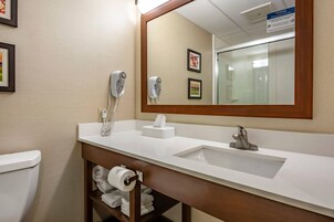 Un baño de hotel con un lavamanos blanco, un espejo, un perchero para toallas y dos secadores de pelo.