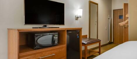 Habitación de hotel con televisión de pantalla plana, microondas, refrigerador, escritorio de madera, silla y armario.