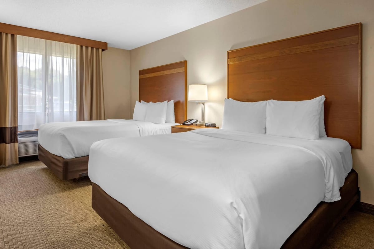 A hotel room with two beds, a bedside table with a lamp, and a window with curtains.