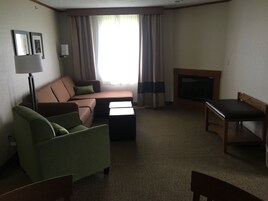 Habitación de hotel con sofá, un sillón verde, una mesa de madera, televisor y lámpara.