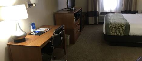 A hotel room with a wooden desk, a chair, a television, a bed, and a window with curtains.