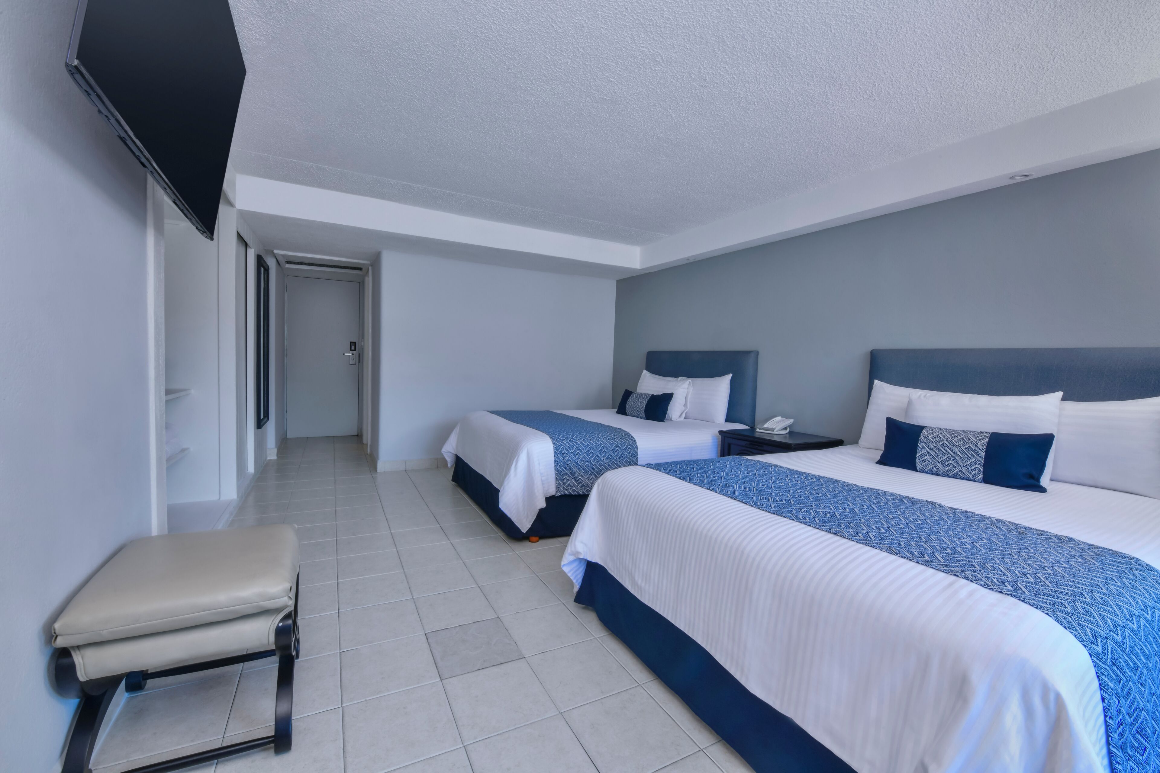 A hotel room with two beds, a bench, and a TV.