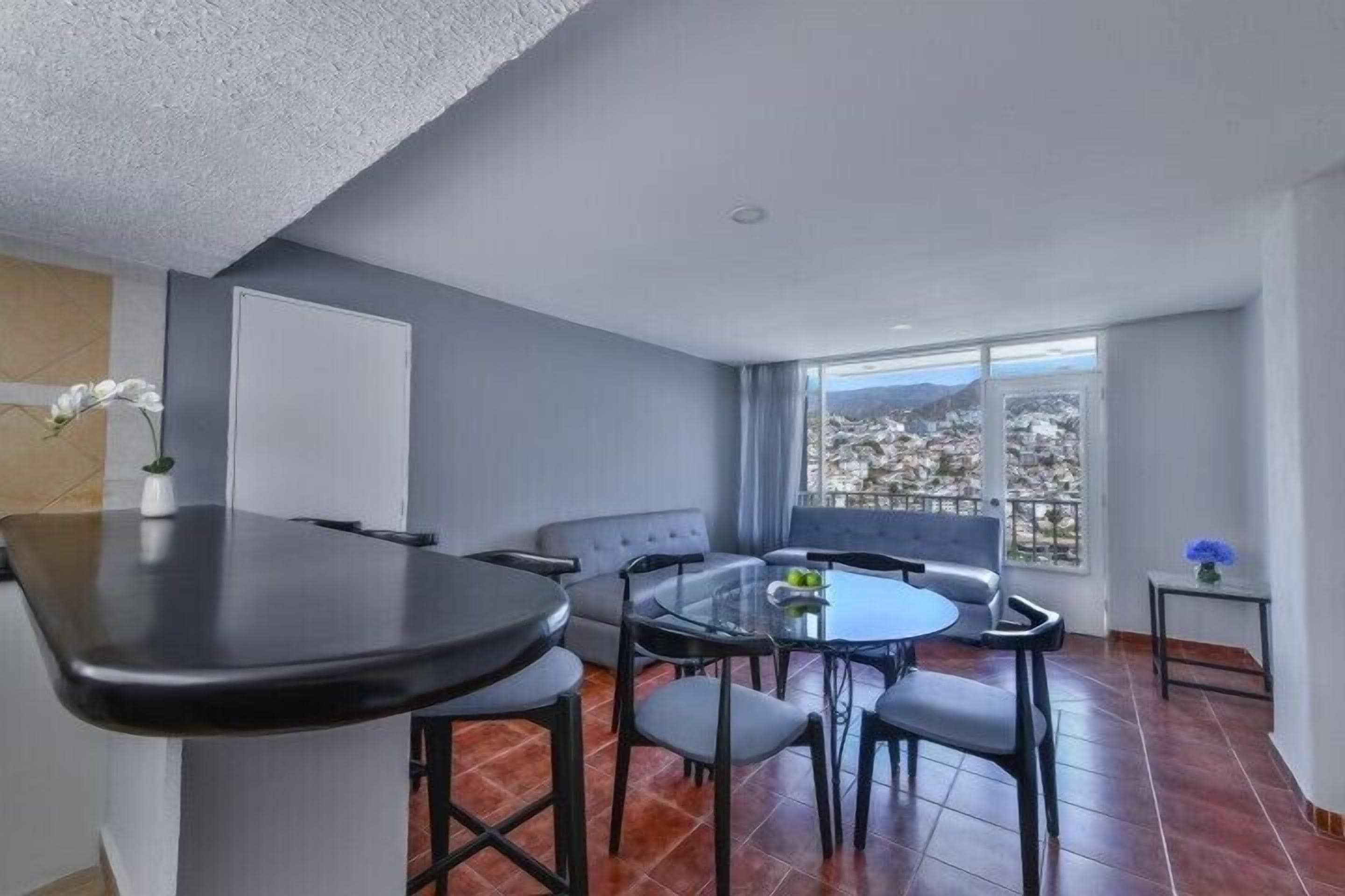 A modern living room with a dining area, large windows, and a view of a cityscape.